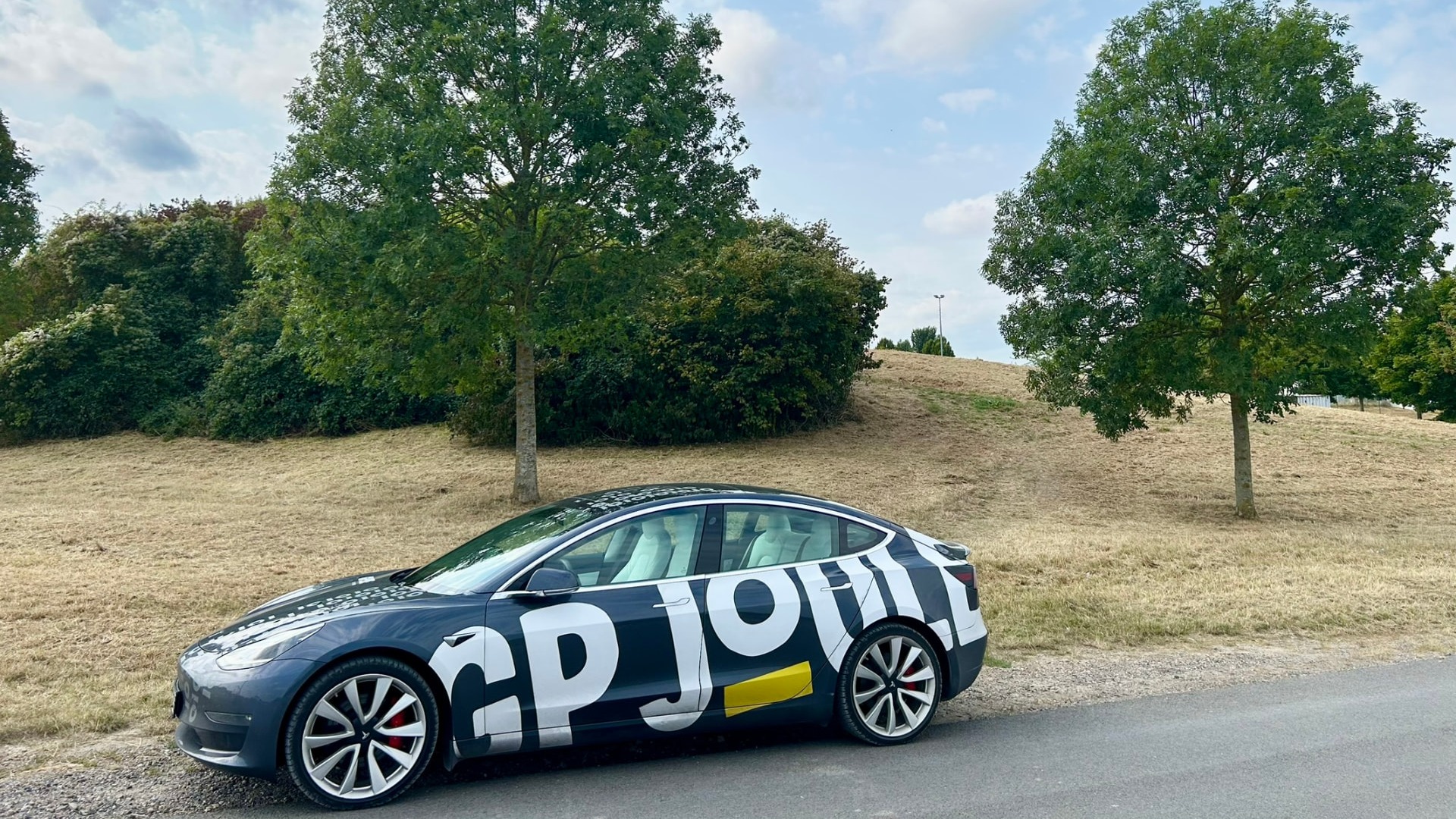 GP JOULE Connect – Tesla mit GP-JOULE-Branding vor Wiese und Bäumen